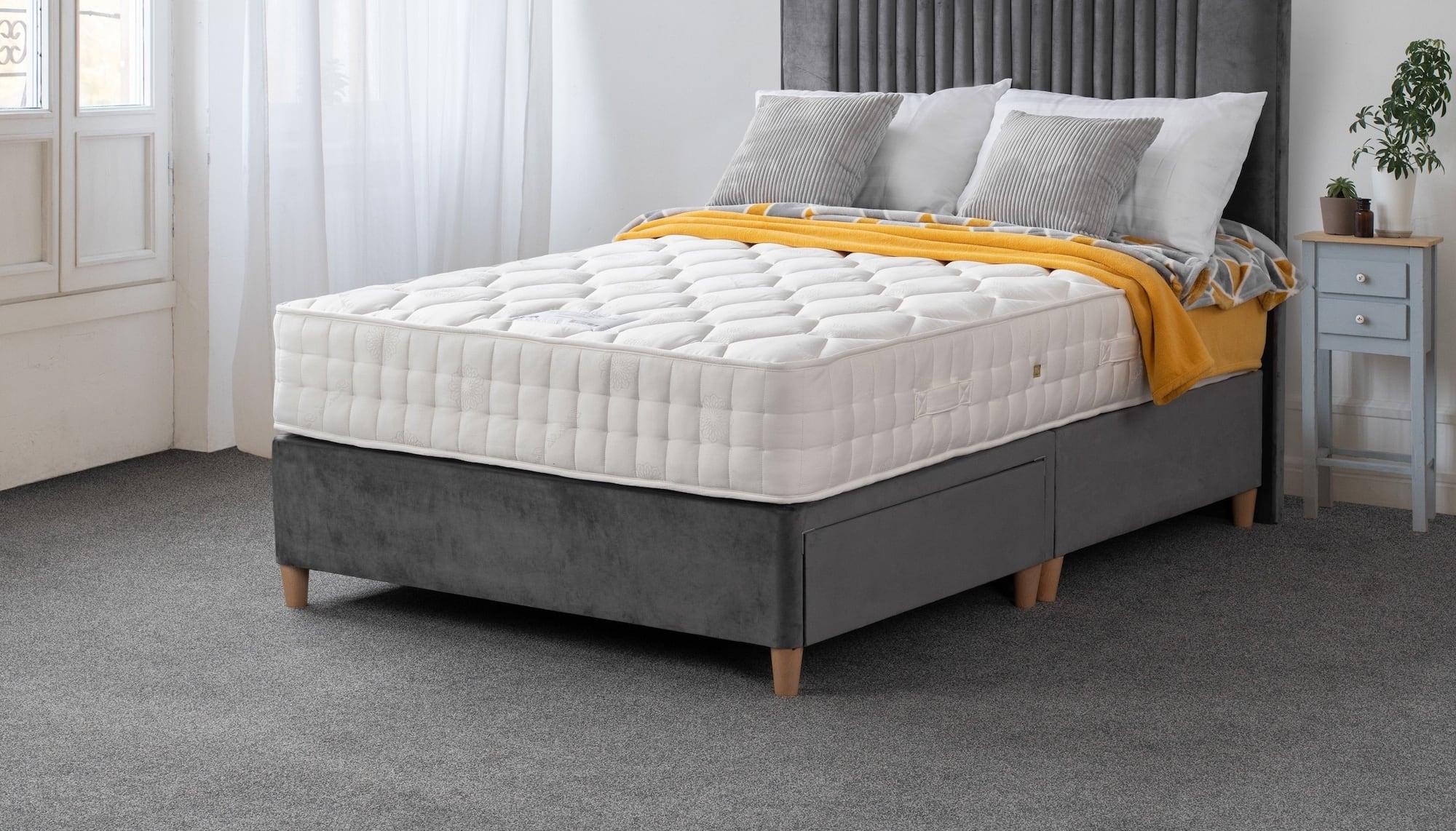 Gray bed frame with white mattress and yellow blanket in a bedroom setting.