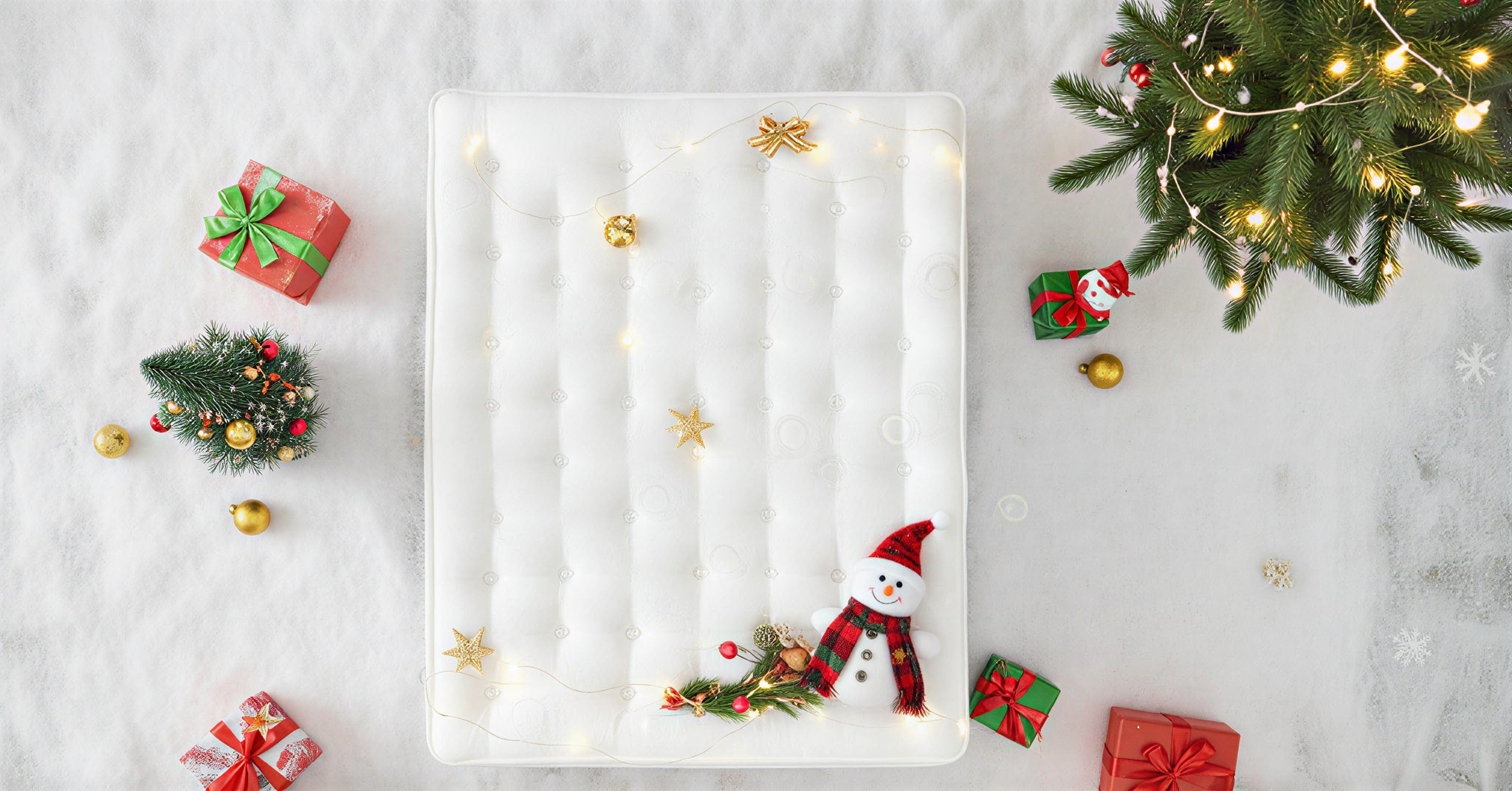 mattress with snowman decoration surrounded by Christmas decorations on a light gray background